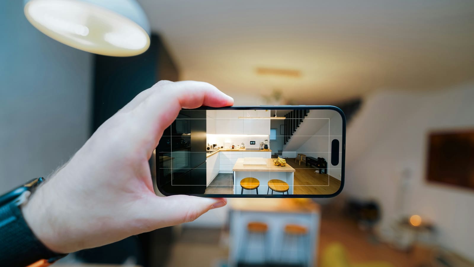 Hand holding a phone to photograph a bright open-plan kitchen and living area