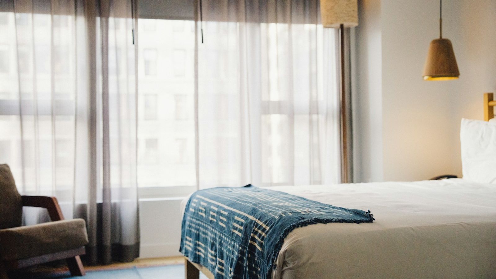 Bright hotel room with a made bed and an armchair by the window