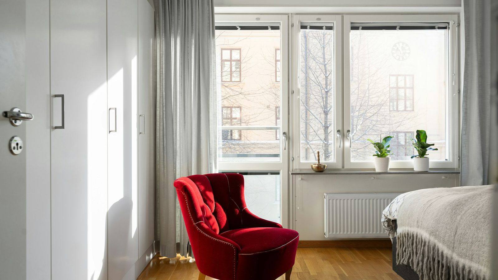 Quiet, empty bedroom with a red armchair by a bright window
