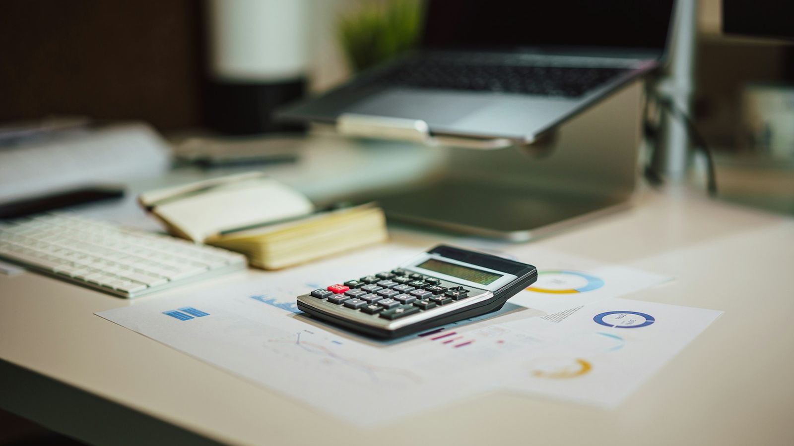 Calculator, notebook and laptop on a desk with financial charts